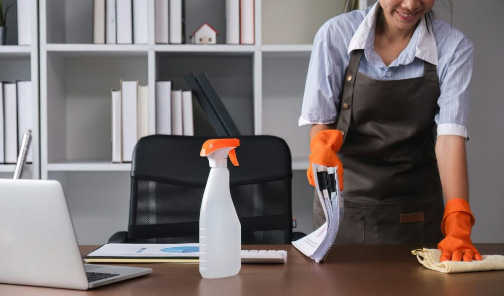 Young woman uses a cleaning cloth to disinfect the computer and equipment on the office table